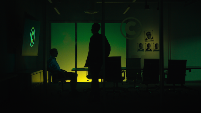 Still from Bitconned: Reenactment scene from the film that features in shadow images Sam "Sorbee" Sharma, Centra Tech's president and co-founder who is seated, and Raymond Trapani, Centra Tech's chief operating officer and co-founder who stands during a discussion about the business in one of the company's offices