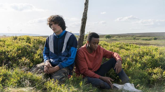 Black Dog: Two teen boys (one White, one Black), sit on the ground in a field