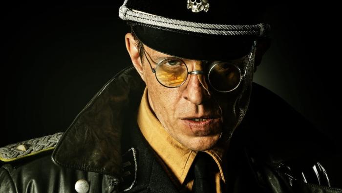 Blood & Gold: Close up of Nazi officer in hat and circle rimmed glasses center