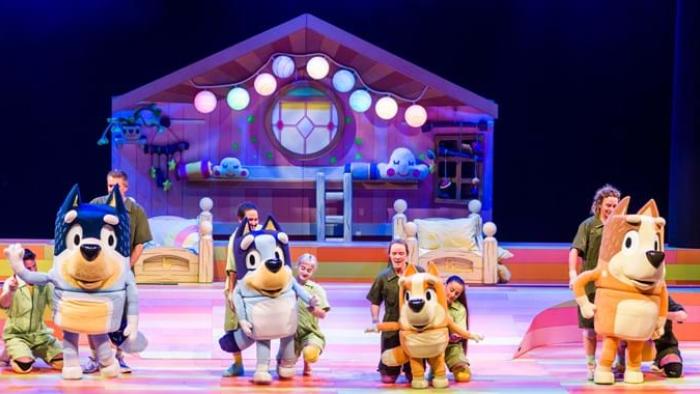 Bluey's Big Play: Bluey’s dad, Bluey, Bingo, and their mom dance in a line on stage with a bedroom lit up behind them