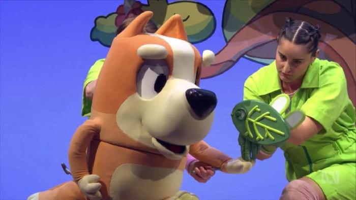 Bluey's Big Play: Bingo holds out her hand to a flying leaf, with puppeteers standing behind her