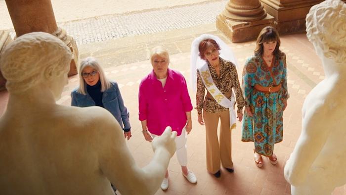 Book Club: The Next Chapter Movie: The main characters, one in a bridal veil and white sash, look at large ancient statues of naked male figures
