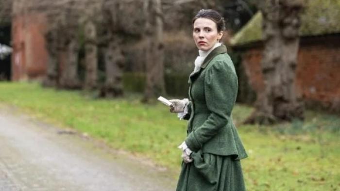 Borley Rectory — The Awakening: A White woman in 1900 clothing looks over her shoulder, concerned, as she walks through the grounds of a manor house