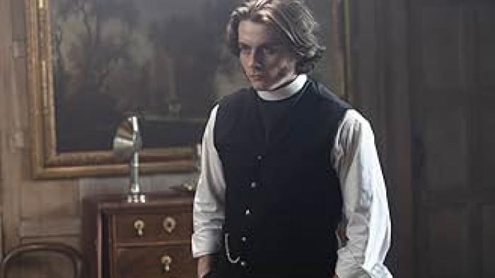 Borley Rectory — The Awakening: A young White man in 1900 clothing stands with his hands in his pockets, looking serious, inside a manor house