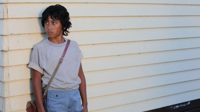 Boy Movie: Boy leans against a white house looking off-screen