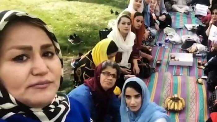 Bread & Roses movie: Afghan woman left holds up cellphone for a selfie with many Afghan women sat behind her, some holding up protest signs