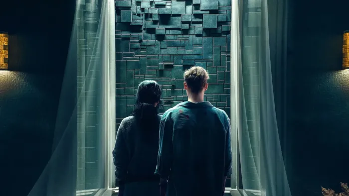 Brick (2025) movie: The backs of German woman left center and German man right center, looking at black bricks that wall up their door opening