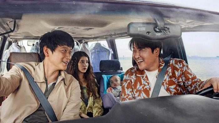 Broker: Two adult Asian men smile in the front seat of a van while a worried looking woman sits in the back seat with a baby