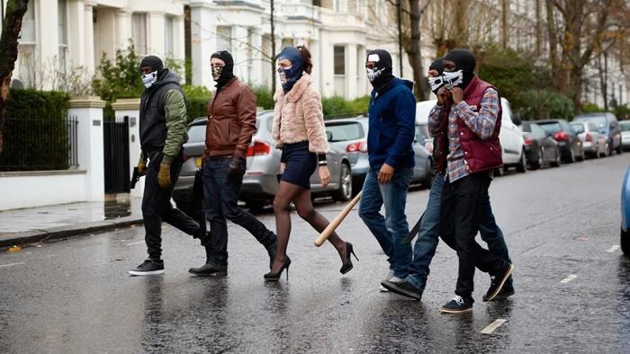 Brotherhood: A group of people in masks walk through a street carrying weapons