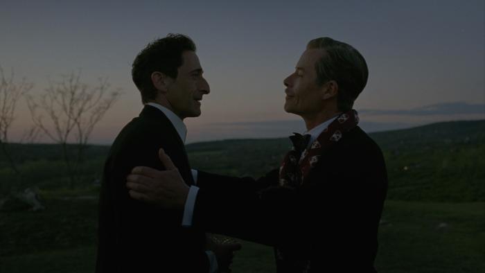 The Brutalist Movie: Harrison Lee Van Buren (Guy Pearce, right) places his hands on László's shoulders