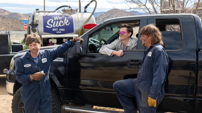 Busboys movie: Two men in dark work jumpsuits stand by a black truck in a desert area