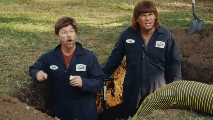 Busboys movie: Two men in dark uniforms stand beside a hole in a grassy area