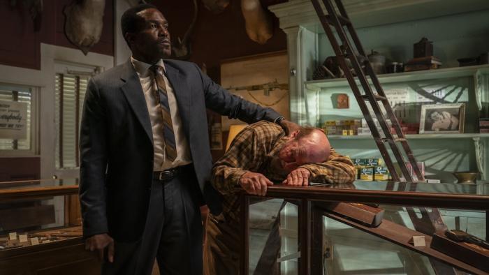 By Any Means Movie: In a gun shop, Strider holds the proprietor's face down on a glass case