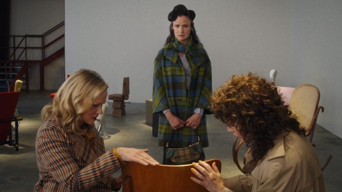 By Design Movie: Camille stands and looks at a beautiful chair as her friends Lisa and Irene touch its wooden surface