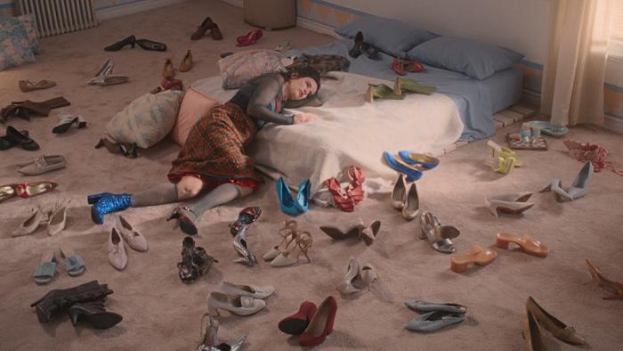 By Design Movie: Camille is slumped at the bottom of her mattress, many pairs of shoes scattered around her