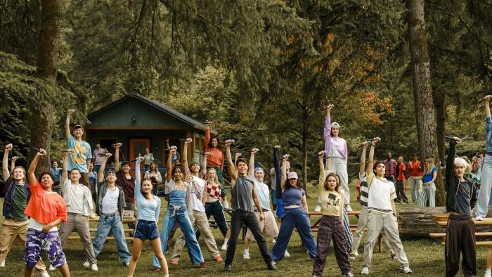 Camp Rock 3 Movie: A large group of campers on Camp Rock pose holding their mics above their hands, smiling after a musical number.