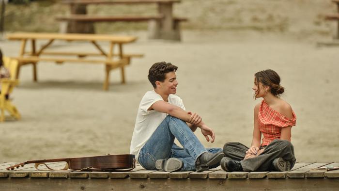 Camp Rock 3 Movie: Fletcher and Sage sit on a dock in a romantic mood, talking and smiling, with a guitar beside them.
