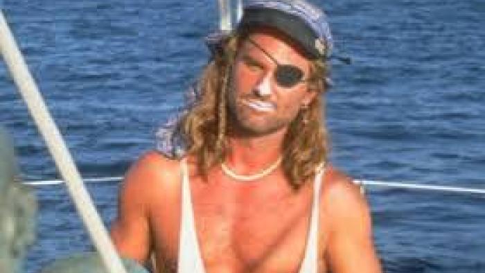 Captain Ron: Kurt Russell with an eye patch on a boat, wearing a bandana and necklace.