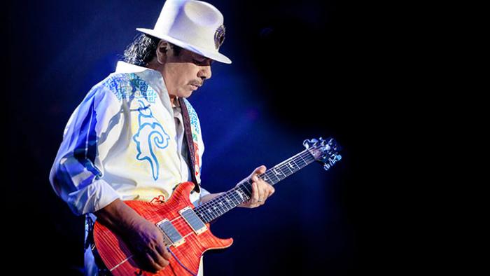 Carlos Movie: Present-day Carlos Santana wears a white outfit and plays guitar during a live show