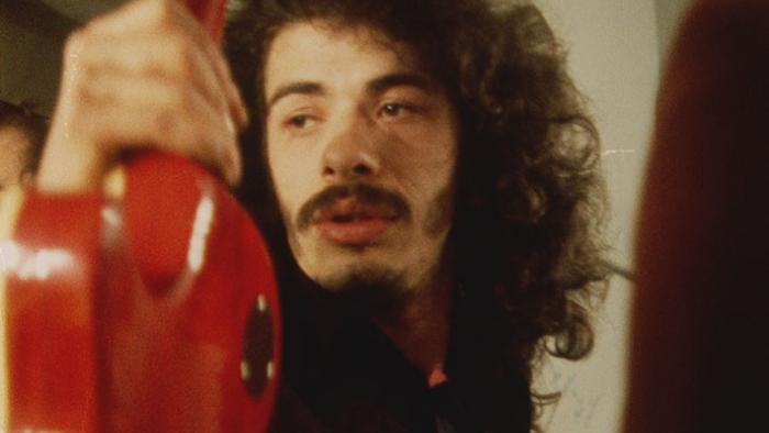 Carlos Movie: Carlos Santana in the 1960s, with long hair and beard, holding a red guitar