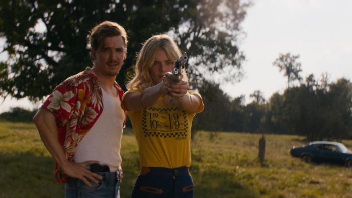 Carolina Caroline movie: Kyle Gallner, in a Hawaiian shirt, watches Samara Weaving shoot a gun during target practice