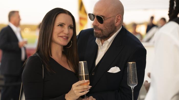 Cash Out Movie: Amelia (Kristin Davis) and Mason (John Travolta), well-dressed and sipping champagne, attend a fancy event