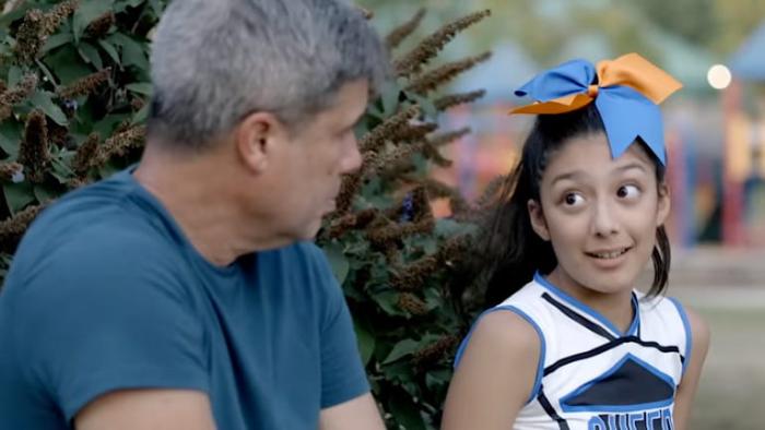 Cheer Dad movie: Joey Victoria Lezama in a cheerleading uniform sits and talks to Tim Perez-Ross at football game