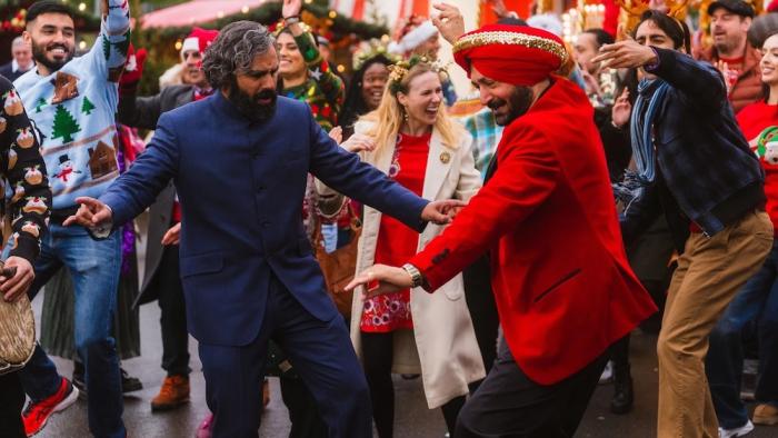 Christmas Karma: Two men dancing together at a festive Christmas party surrounded by celebrating crowd in holiday attire