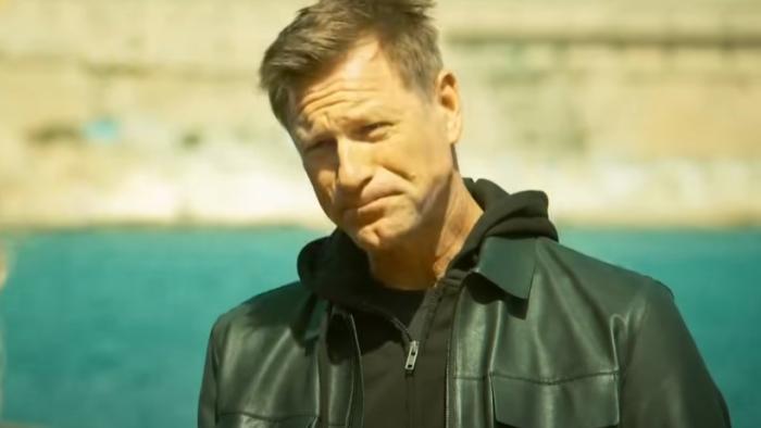 Classified movie: Aaron Eckhart in black leather jacket center smirks while outside in the sun