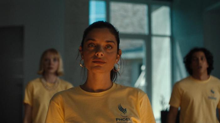 Corporate Retreat Movie: Ginger (Odeya Rush) stands defiantly in front of two others, all wearing identical yellow T-shirts