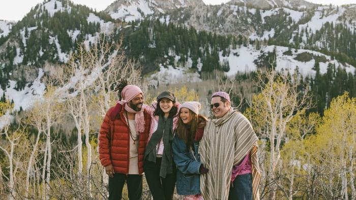 Couples Weekend movie: Daveed Diggs, Alexandra Daddario, Josh Gad, and Ashley Park stand together smiling in winter coats