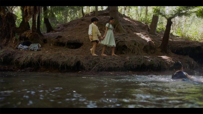 Cousins Movie: Two girls hold hands while walking barefoot on a riverbank
