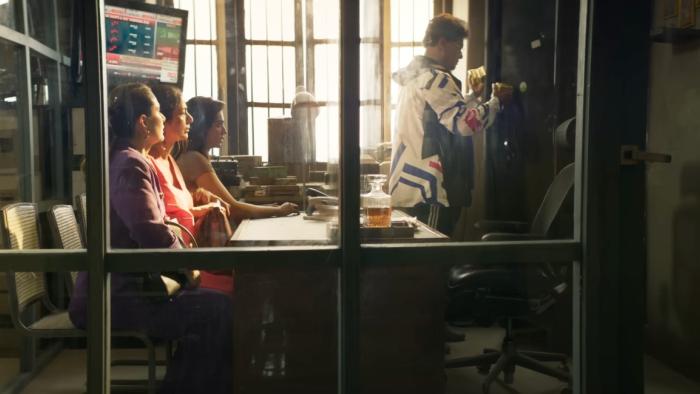 Crew: Three characters sit together in an office where someone is taking out gold for them to smuggle