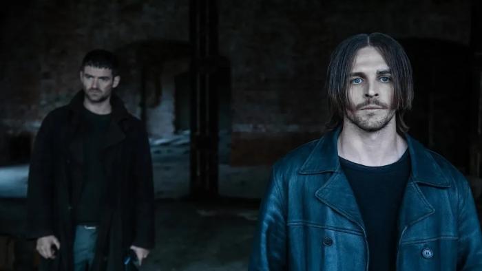 Dampyr: Two White men stand in a deserted brick building surrounded by darkness