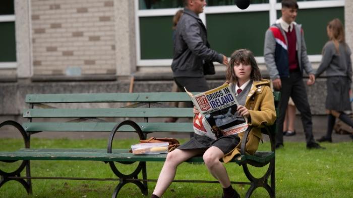 Dating Amber movie: Amber sits on a bench holding a newspaper with headline DRUGS IN IRELAND