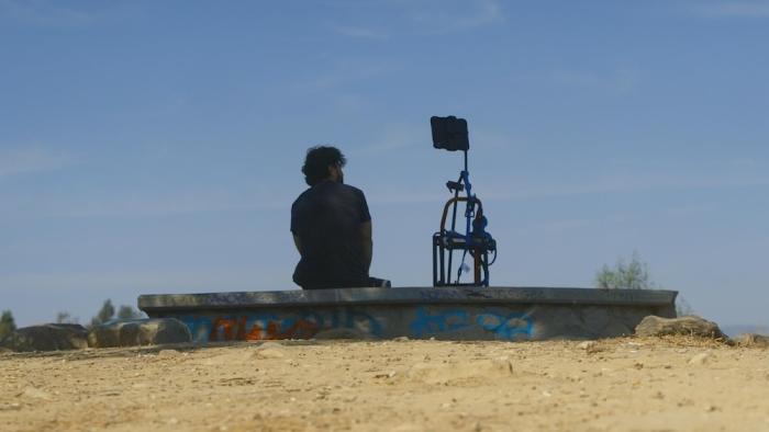 Deepfaking Sam Altman Movie: Seen from behind, Adam seems to be conversing with "Sambot," mounted on a kind of tripod