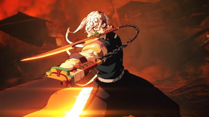 Demon Slayer - To the Swordsmith Village movie: A member of the demon slayer corps is shown holding a sword in their mouth and swinging another sword, behind him a burning village can be seen