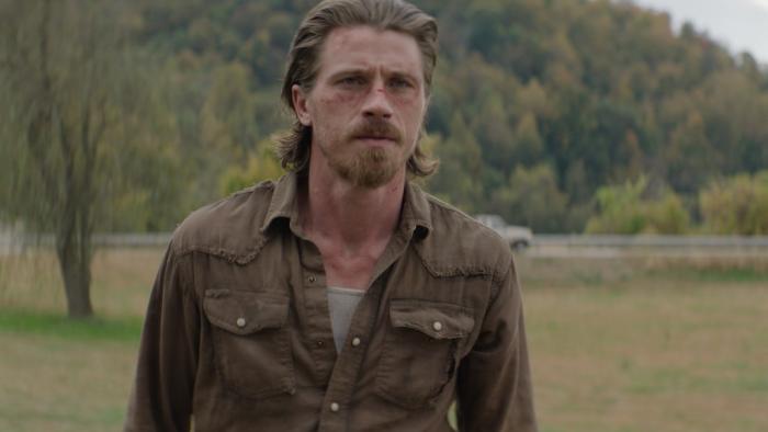 Desperation Road Movie: Russell (Garrett Hedlund) stands somewhere outdoors, his face bruised and scraped, looking grim