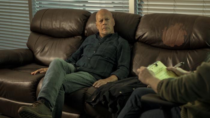 Detective Knight: Independence Movie: Bruce Willis sits on a couch while speaking to a therapist, who partly appears on the right