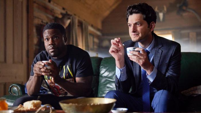 Die Hart 2: Die Harter movie: Kevin Hart left and Ben Schwartz right sit on couch and drink tea in front of coffee table