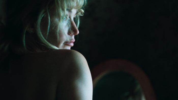 Die My Love movie: Jennifer Lawrence looks over her bare shoulder in a dark room