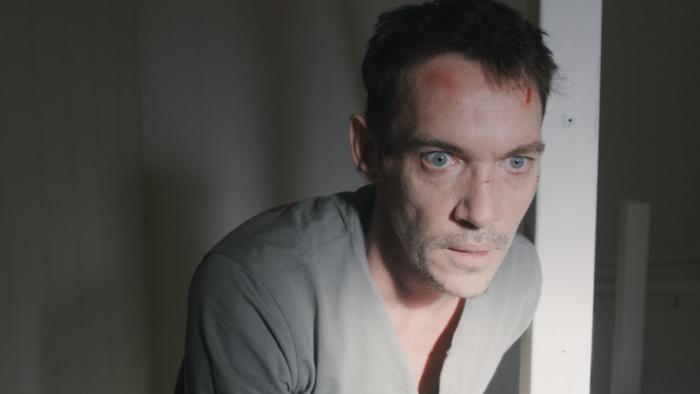 Disquiet Movie: Jonathan Rhys Meyers stands in a doorway looking shocked, and there are cuts and bruises on his forehead