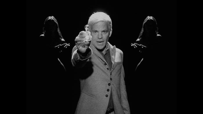 Divinity Movie: Jaxxon Pierce holds a bottle of "Divinity" up to the camera in an advertisement for the anti-aging drug