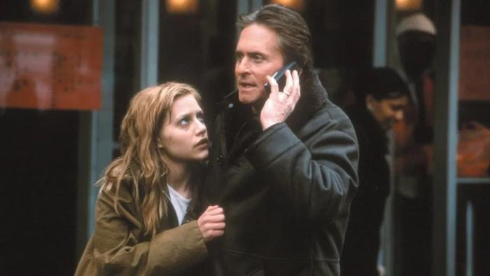 Don't Say a Word movie: Nathan talks on a cell phone while Elizabeth clutches his jacket and looks up at him worriedly.