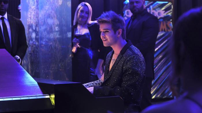 Double Trouble movie: Pop star Juniper (Jack Griffo) plays piano and sings in a nightclub wearing a diamond arm gauntlet