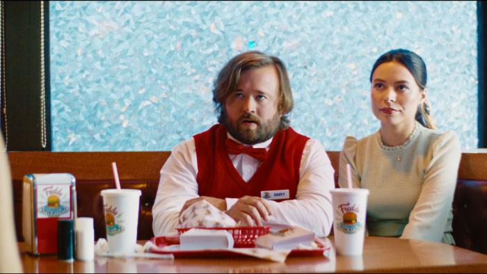 Drugstore June: A couple sits at a fast food booth looking up with contempt  at a person who stopped at their table