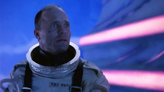 The Abyss Movie: Ed Harris wears a deep-sea diving suit with the helmet off against a neon blue and pink backdrop