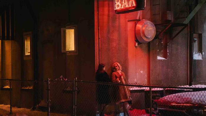 Eileen Movie: Two women speak outside a bar in the glow of red neon lights