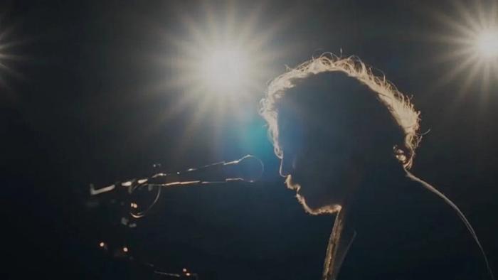Elijah Peel movie: Malcolm Cumming sings into a mic, a bright spotlight shining on him