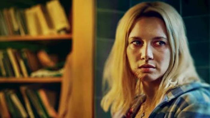 Elize: Shadows of a Woman movie: Woman with blonde hair in flannel shirt, with a bookshelf in the background.